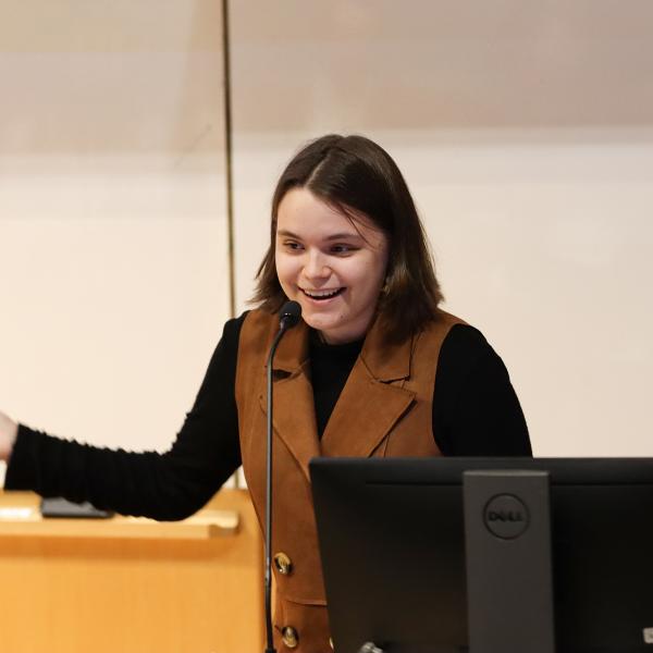 A student holds their right arm out and smiles.